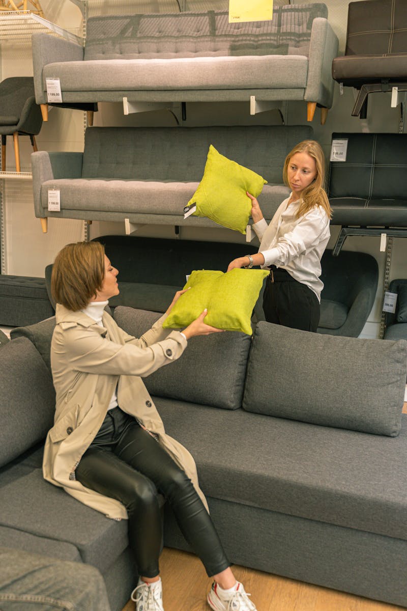 Two women choosing green cushions in a modern furniture store, enjoying shopping.